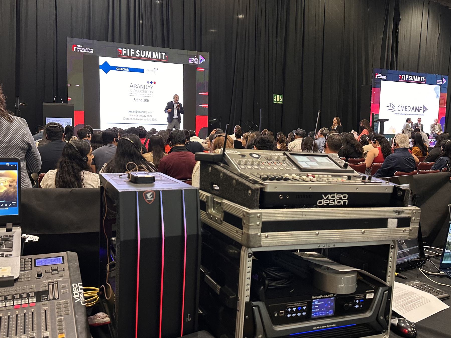Consola y equipo de audio en el piso de un summit corporativo con audiencia
